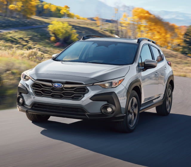 Subaru Crosstrek drives on a winding road through a scenic landscape, with vibrant autumn trees and mountains in the background.