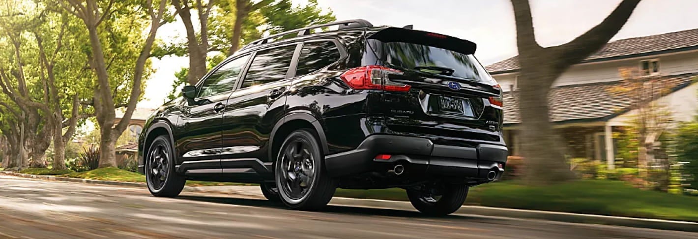 Black Subaru Ascent driving along a tree-lined residential street, shown from the rear three-quarter angle.
