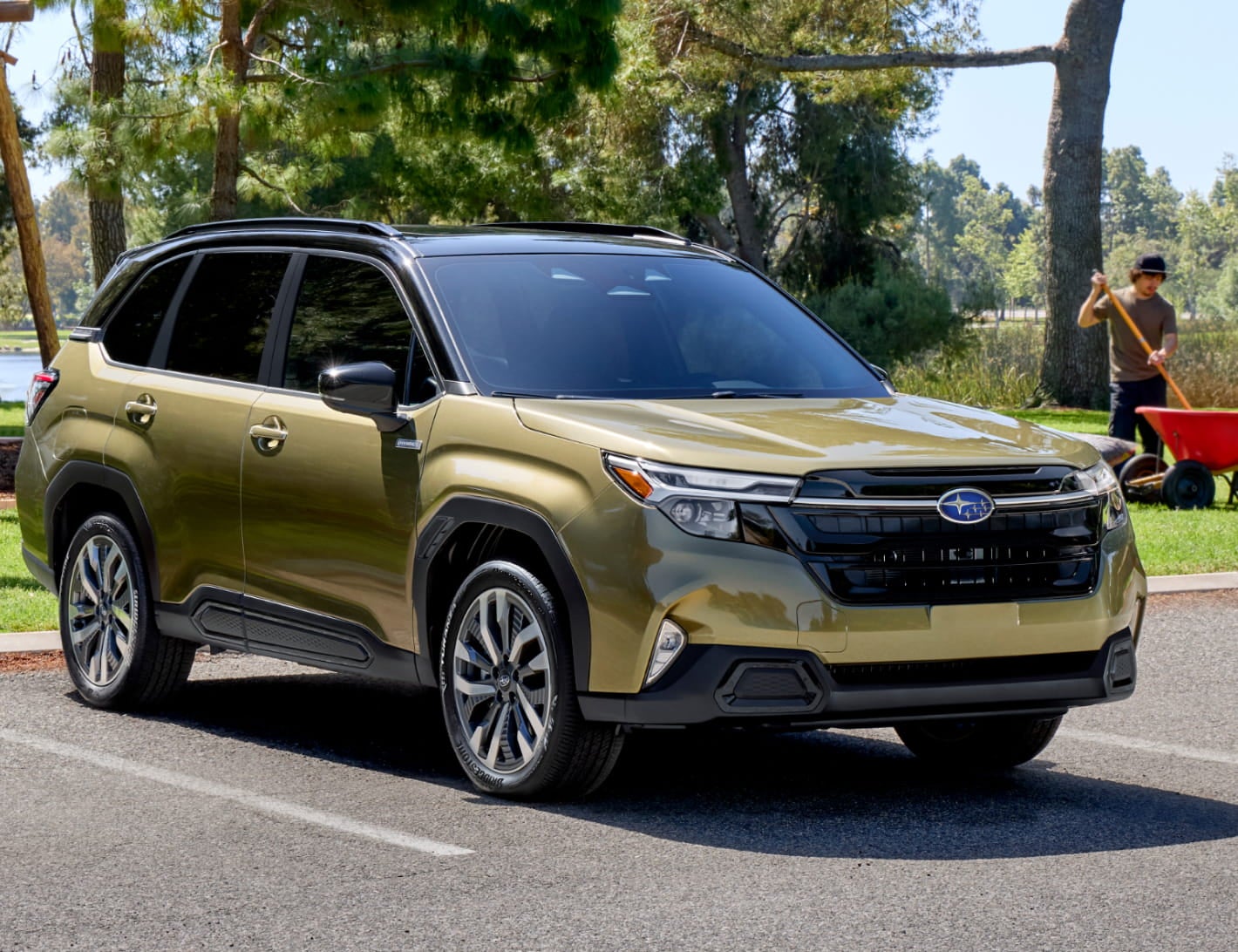 Green Subaru Forester Hybrid parked near a wooded park with a person working in the background.