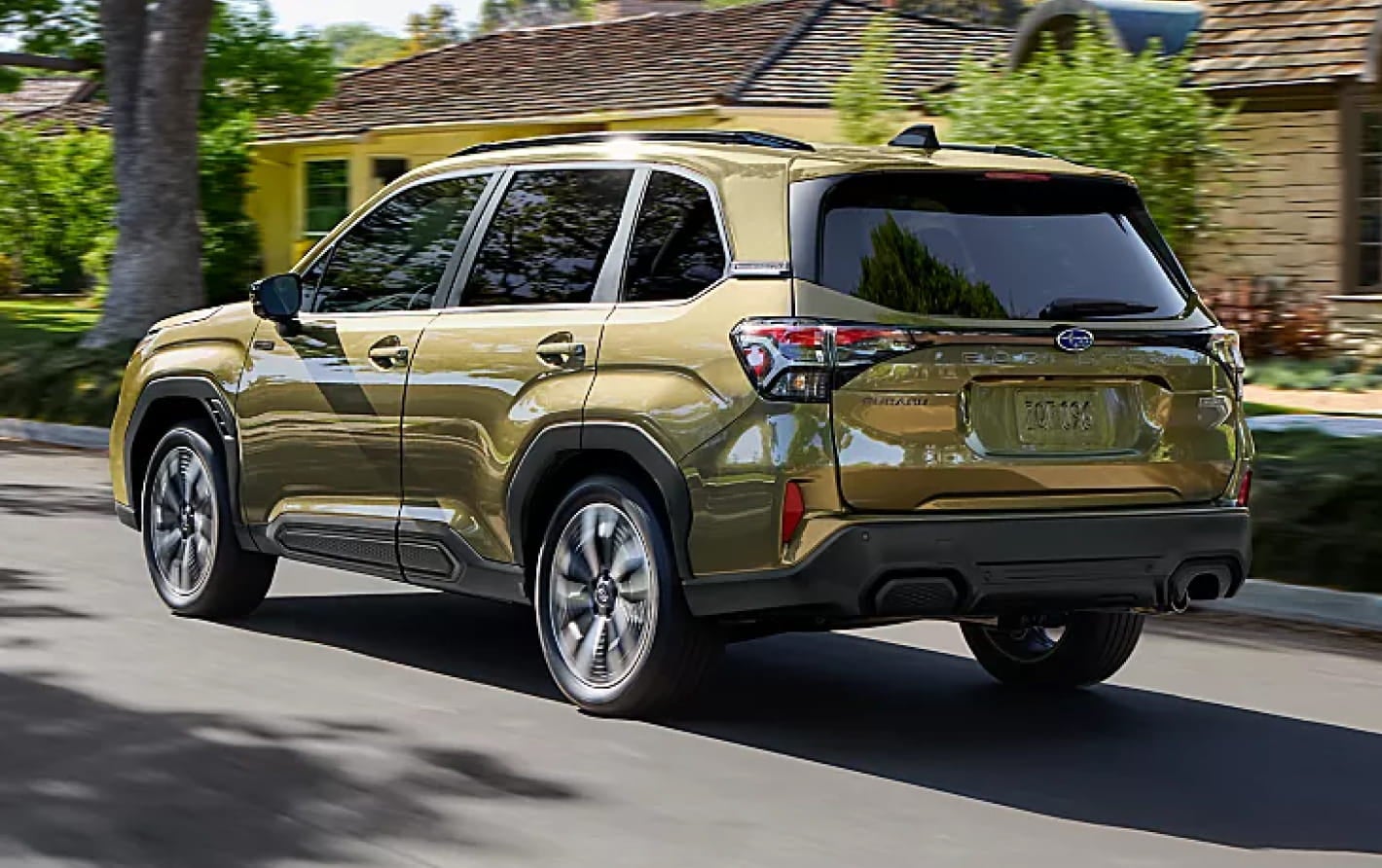 Green Subaru Forester Hybrid driving through a residential neighborhood, shown from the rear three-quarter view.